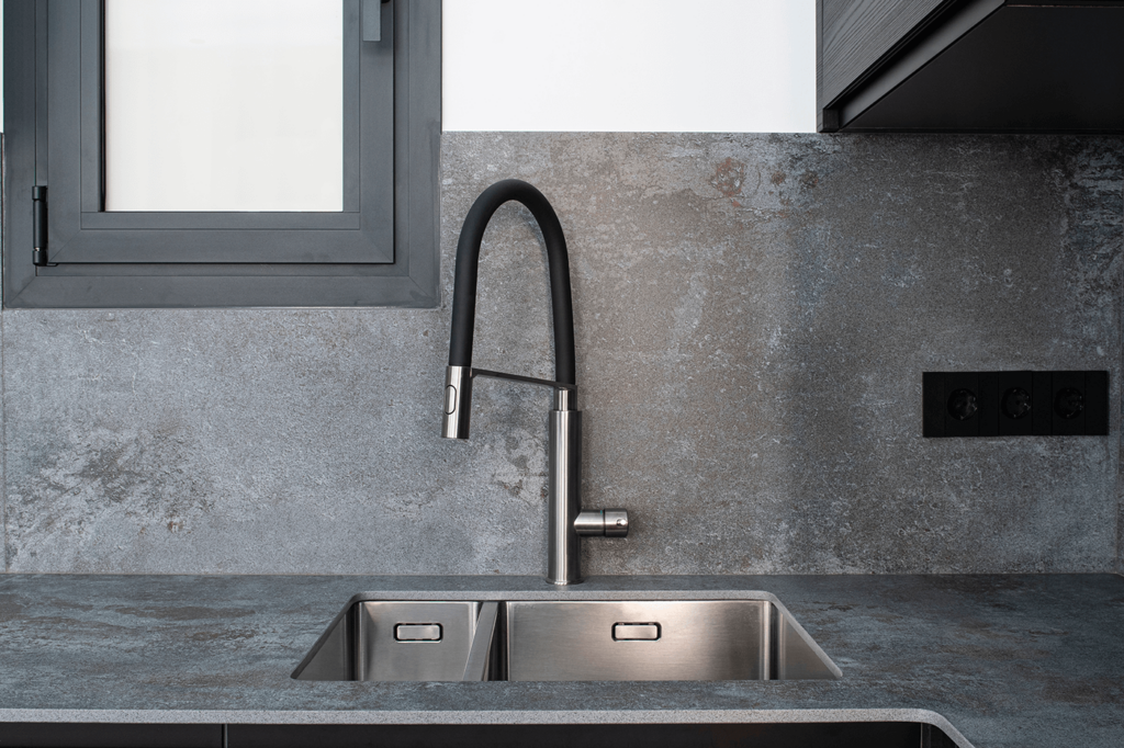 Doppelspülbecken aus Edelstahl mit schwarzem, gebogenem Küchenwasserhahn vor grauer Wand.