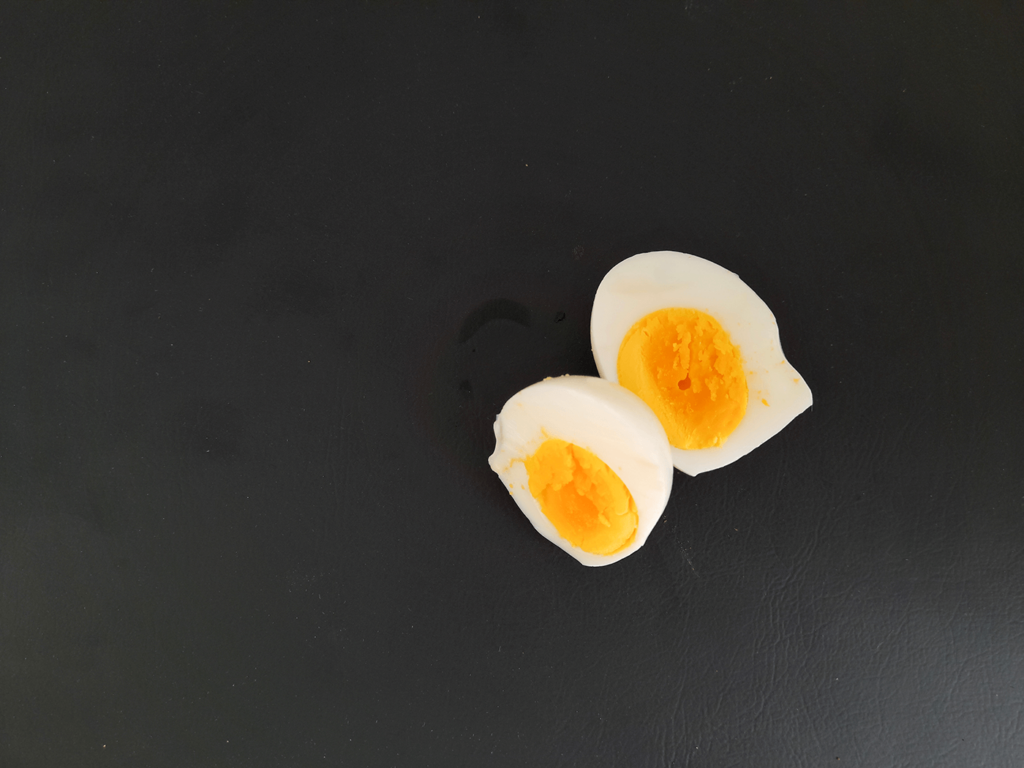 Zwei Hälften eines gekochten Eis mit gelbem Eigelb auf dunklem Untergrund.