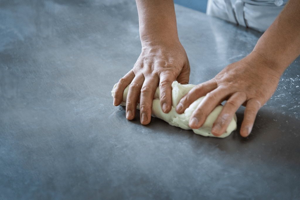 Hände kneten einen Teig auf einer glatten Arbeitsfläche.